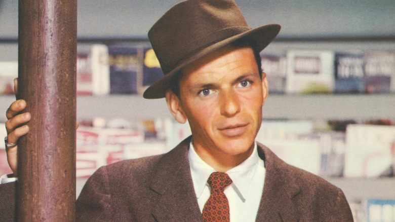 Young Frank Sinatra wearing a fedora and holding onto a round column.