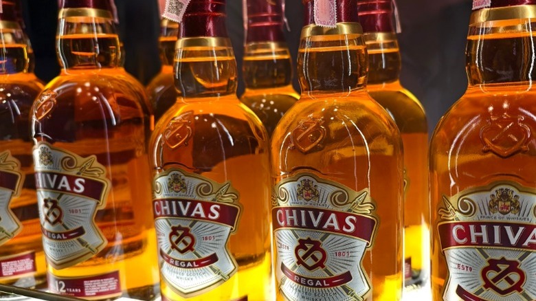 Bottles of Chivas Regal lined up on a store shelf.