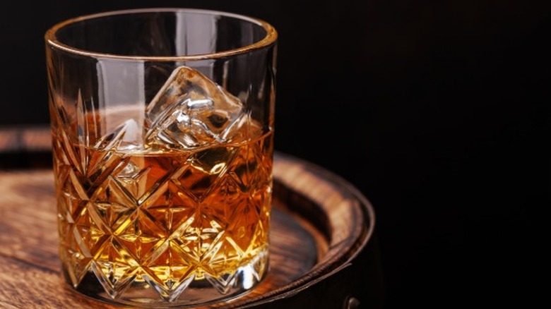 A glass of whiskey on the rocks in a ricks glass sitting atop a barrel.