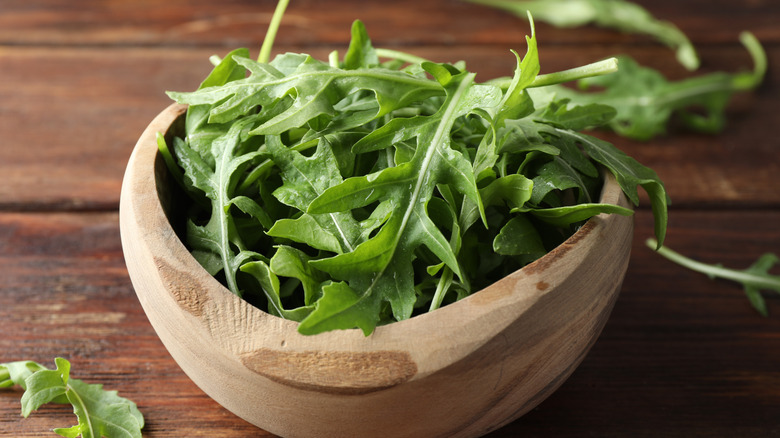 A bowl of arugula is on a wooden table.