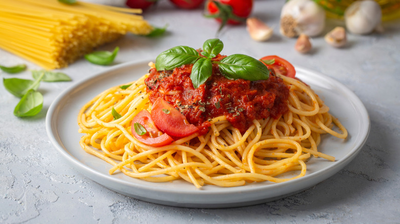 A plate of spaghetti with marinara on a table with ingredients in the background