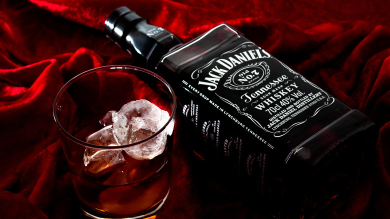 A bottle of Jack Daniel's Tennessee whiskey on its side on red velvet, a rocks glass with whiskey sitting next to it.