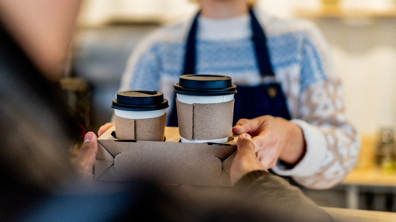 A woman in an apron hands a man a tray full of two to-go cups.