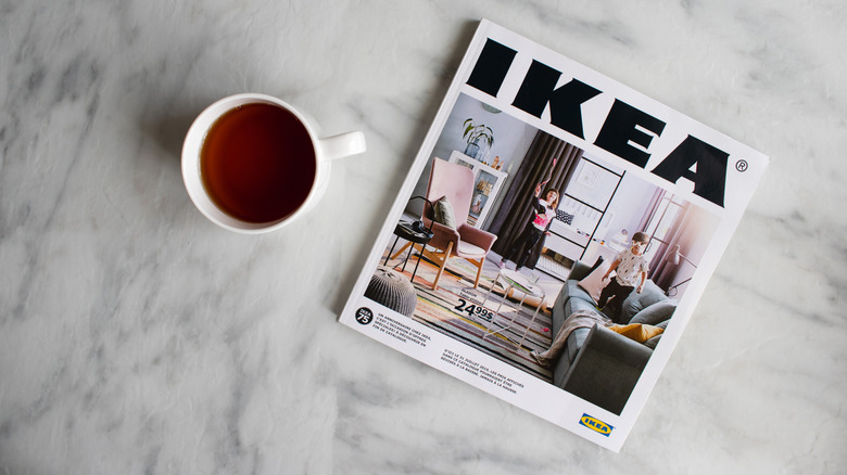 A cup of tea sits beside an Ikea catalog on a white countertop.
