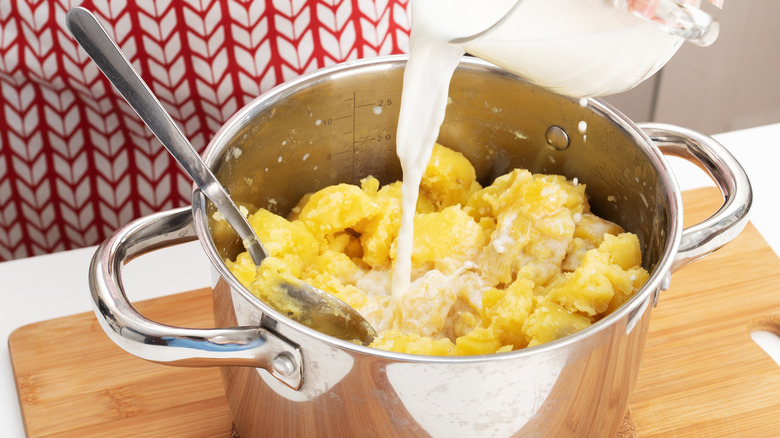 Person pouring milk into pot of mashed potatoes