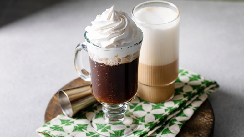 Two clear glasses with coffee, whipped cream, and foam over a green and white cloth napkin
