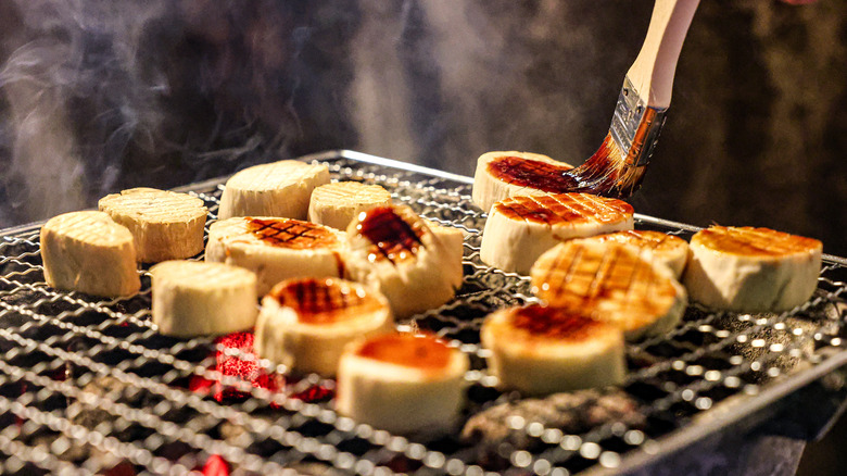 Tofu medallions are brushed with a marinade as they cook on a grill.