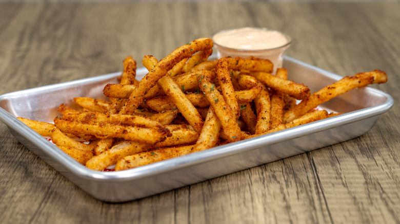 Dish of seasoned fries with a bowl of dip on the side