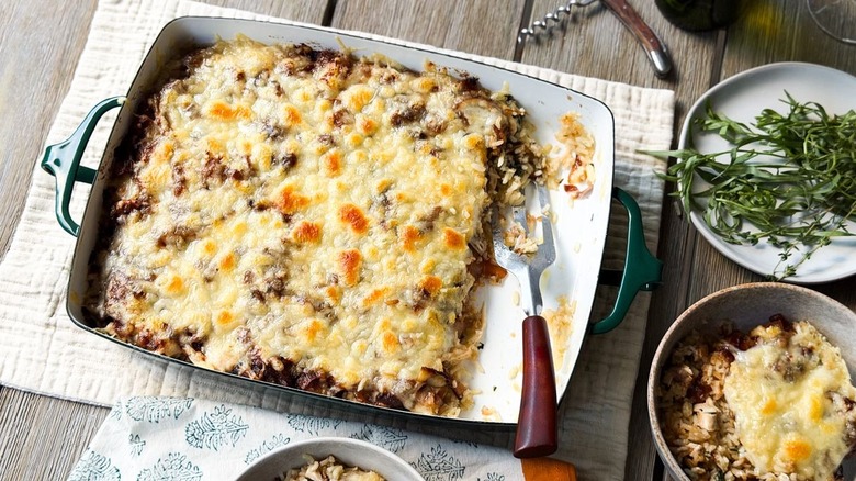 French onion chicken and rice casserole in serving dish and bowl on table with fresh tarragon and corkscrew