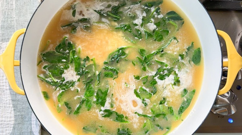 Spinach and white rice in chicken stock in large pot on stovetop