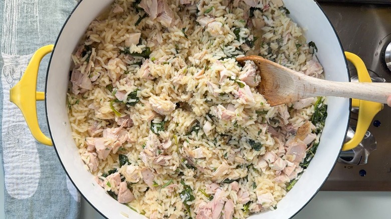 Stirring chicken, rice, and spinach in large pot with wooden spoon