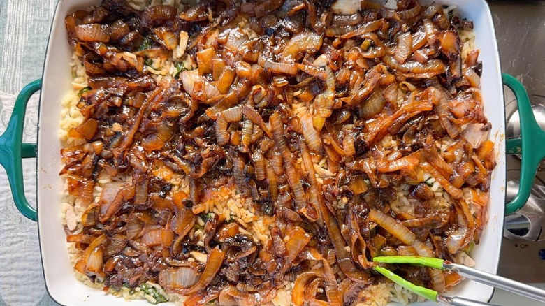 Placing caramelized onions over chicken and rice with tongs in baking dish