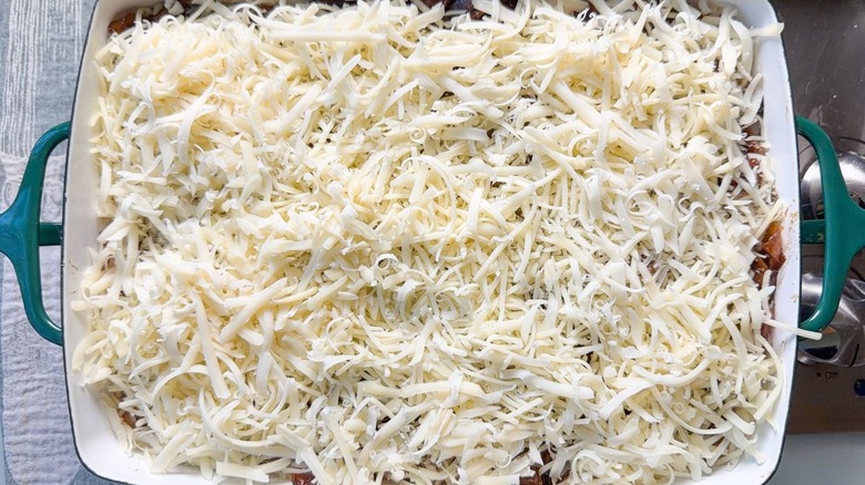 Shredded Gruyère cheese on top of French onion chicken and rice casserole in baking dish