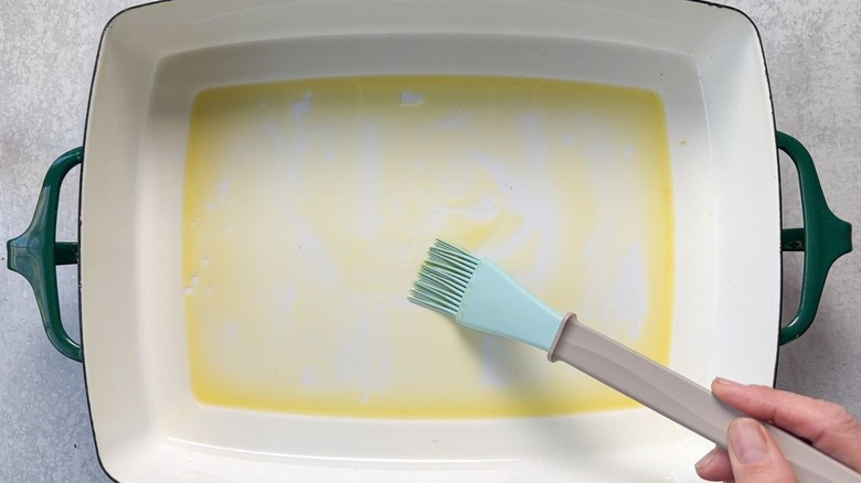 Brushing olive oil on the inside of a baking dish using a pastry brush