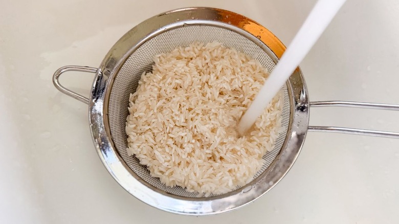 Rinsing white rice in mesh strainer with water in sink