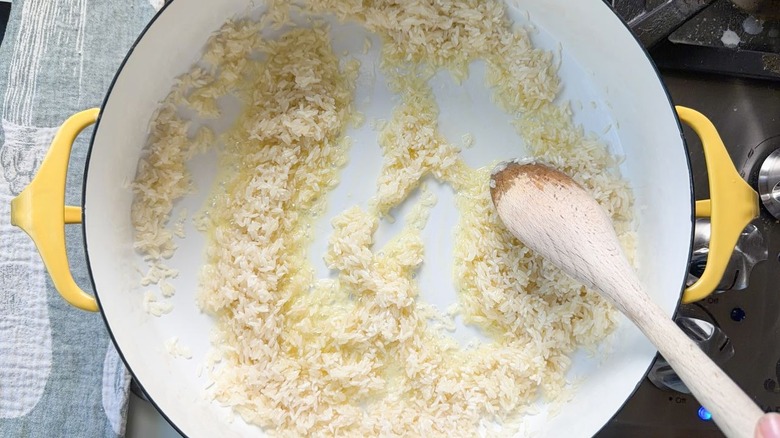 Stirring white rice grains in butter and oil in large pot on stovetop with wooden spoon