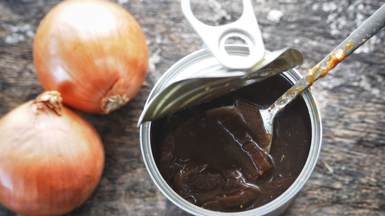 An opened can of French onion soup sits next to two whole onions
