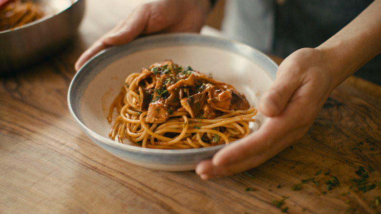 An individual holding a bowl of spaghetti.