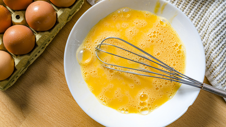 Beaten eggs are in a bowl with a whisk,