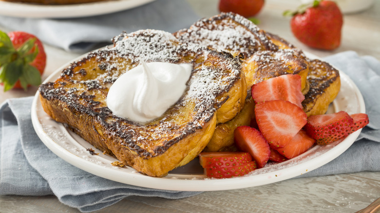 A plate of French toast with strawberries and whipped cream.