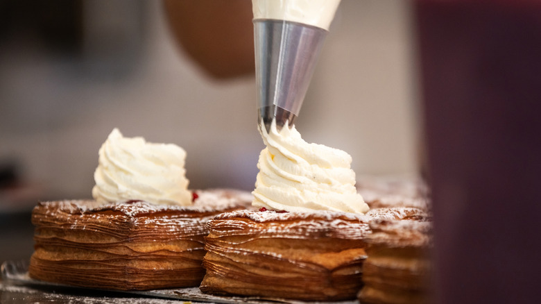 someone pipes cream onto a flaky pastry