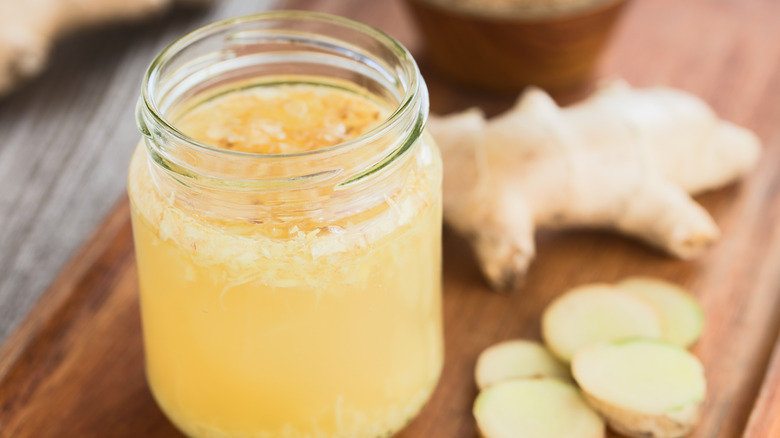A jar of ginger bug on a wooden cutting board surrounded by fresh ginger
