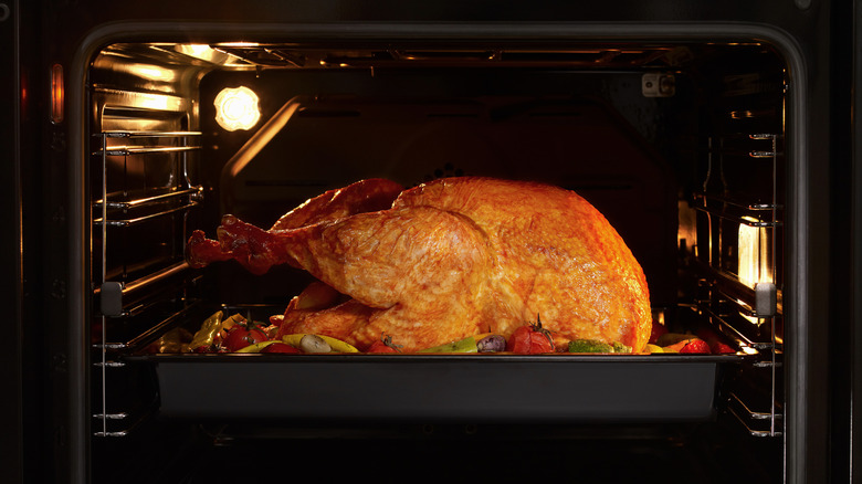 A whole turkey in a tray with vegetables in an oven