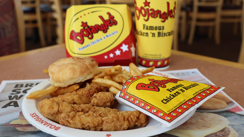 a plate of Bojangles fried chicken, fries, and a biscuit with a cup and box behind them