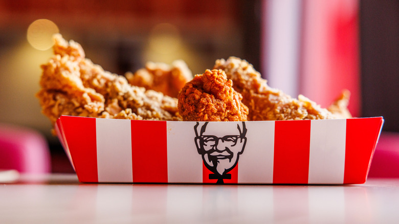 red and white box of KFC fried chicken with the colonel's face front and center, with blurred background