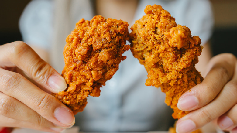 a person holding two pieces of fried chicken, one in each hand, with their body blurred in background