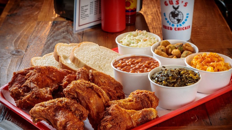 a red platter of fried chicken, traditional Southern sides like collard greens, and a Gus's drink cup in the background