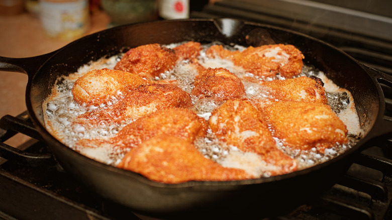 Multiple pieces of chicken fry on a cast iron skillet