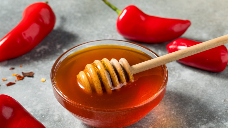 Glass bowl of honey with a honey dipper and chili peppers in the background