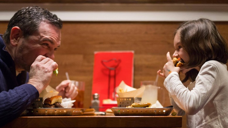 Father and daughter sitting across a table from each other biting into sandwiches at Chili's Grill & Bar