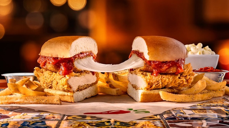 Chicken Parm Big Crispy sandwich cut in half with mozzaralla cheese pulled between the two sandwich halves surrounded by seasoned fries
