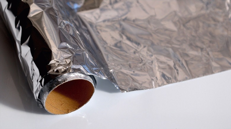 Partially unrolled tube of aluminum foil over a neutral background