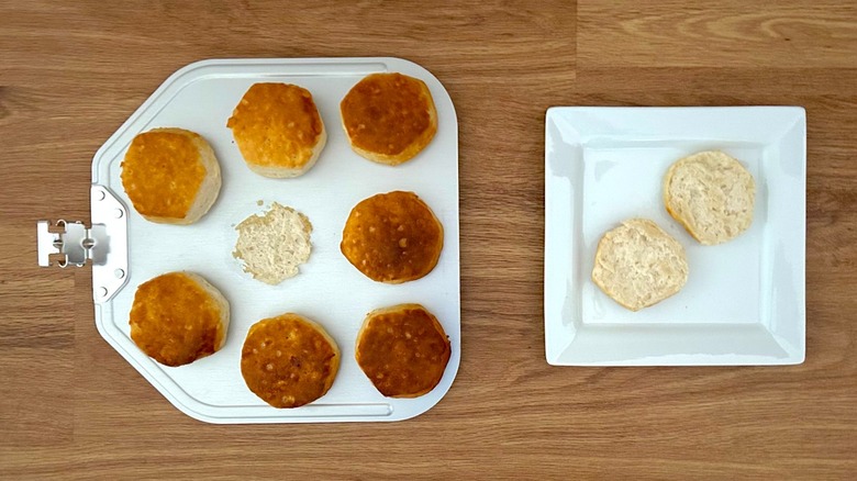 Baked biscuits on a pizza peel and a biscuit cut in half on a square white plate