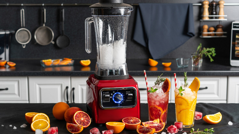 Blender in kitchen with citrus drinks and ice