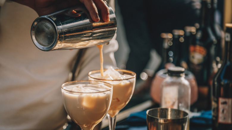 person pouring cocktail into two glasses