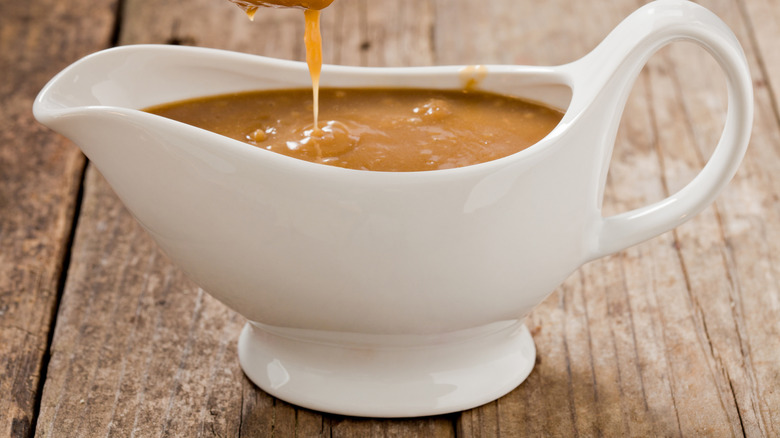 Brown gravy pouring into a white ceramic gravy boat.