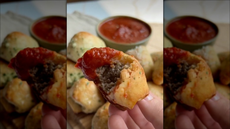 Woman holding half bitten meatball bomb dipped in marinara sauce.