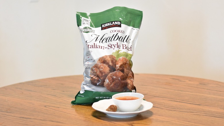 A bag of Kirkland Signature meatballs next to a meatball and marinara on a white plate