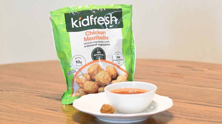 A bag of KidFresh chicken meatballs next to a meatball and marinara on a white plate