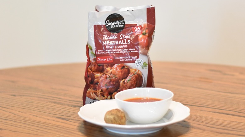 A bag of Signature Select meatballs next to a meatball and marinara on a white plate