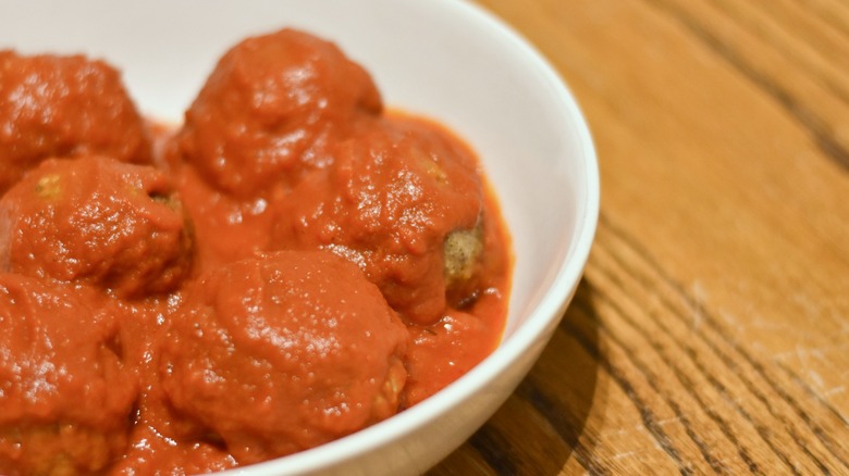 Meatballs in red sauce in a white bowl on a wooden table