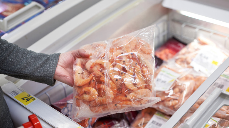 Person taking a package of frozen shrimp out of a freezer at a grocery store