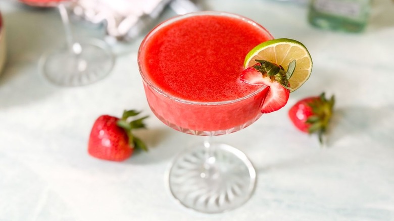 Frozen strawberry daiquiri in coupe glass with strawberry and lime garnish
