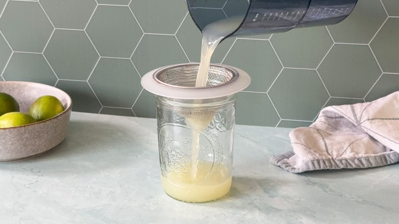 Straining fresh lime juice into a glass jar
