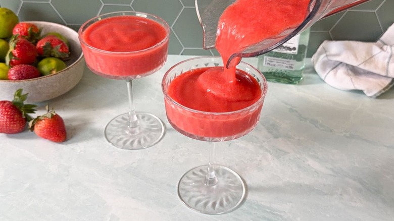 Pouring frozen strawberry daiquiri mix from blender pitcher into chilled coupe glasses