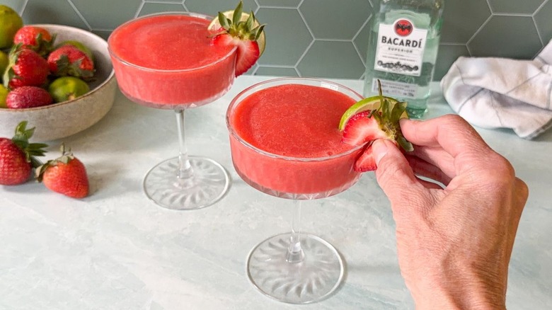 Garnishing frozen strawberry daiquiris in coupe glasses with strawberries and lime wheels